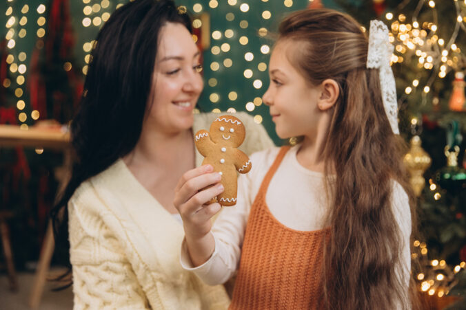 Mother and daughter sharing christmas gingerbread cookie near decorated tree