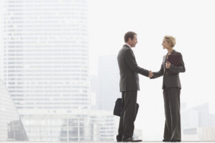 Two businesspeople outdoors shaking hands at top of staircase