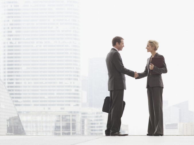 Two businesspeople outdoors shaking hands at top of staircase