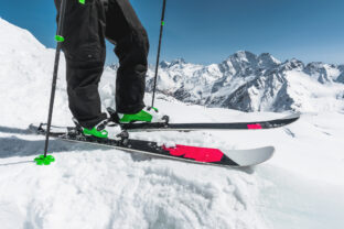 A close up of the ski on the athlete's feet against the background of snow capped rocky mountains. The concept of winter sports in the mountains