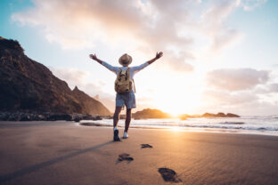 Young man arms outstretched by the sea at sunrise enjoying freedom and life, people travel wellbeing concept