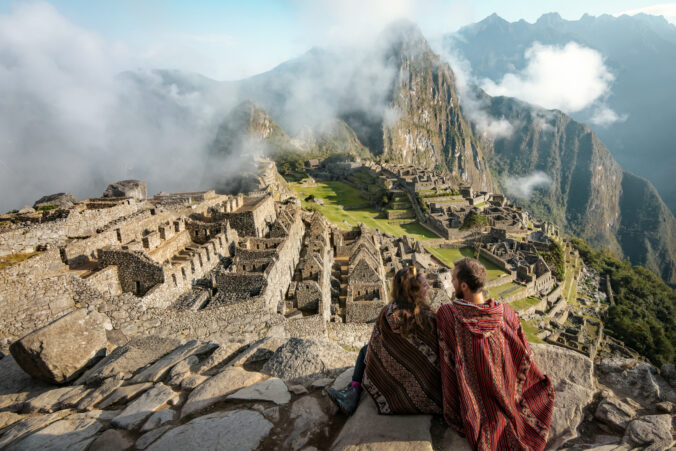 Couple dressed in ponchos watching the ruins of Machu Picchu, Peru