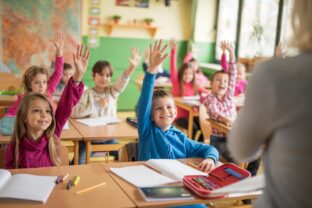 School children raising their hands ready to answer the question.