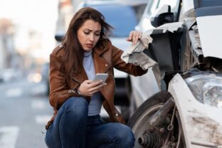 Displeased woman dialing for help after a car accident in the city.