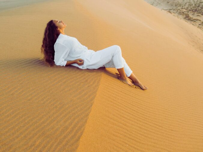 Beautiful brunette woman in white clothes relaxing on top of sand dune.jpg