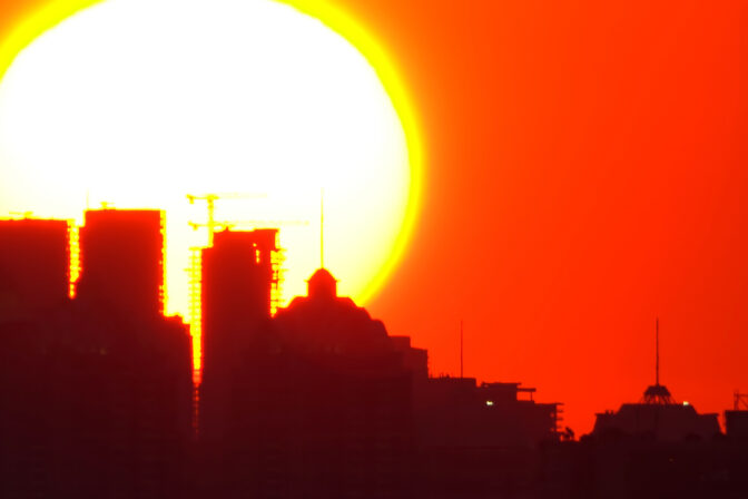 Extrémne počasie: Silueta mesta počas intenzívneho západu slnka s istotou teplom, ktoré symbolizuje dopady klimatických zmien a extrémnych horúčav.