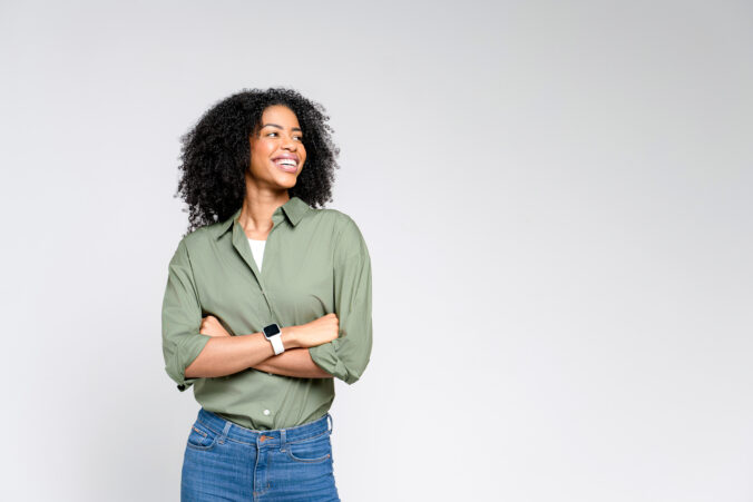 A confident African American woman in a casual olive green shirt and jeans stands with a beaming smile