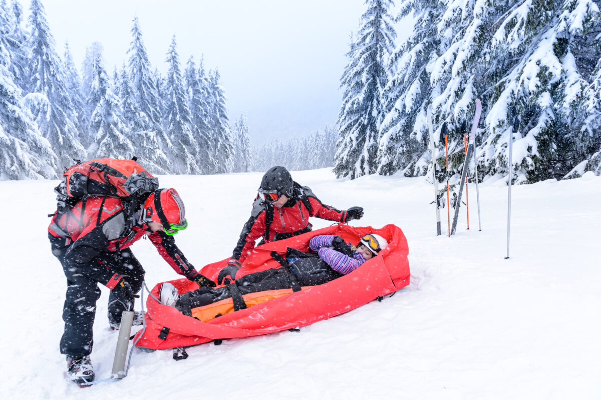 Rescue of injured woman by ski patrol sled on snowy mountain