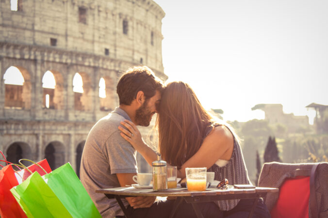 Romantic happy couple young tourists in love kissing cuddling at restaurant in front of colosseum in rome at sunset with lens flare