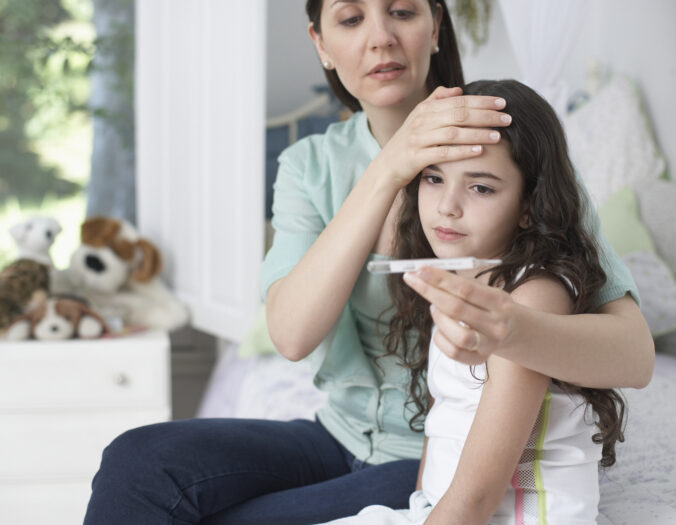 Woman in bedroom taking young girls temperature