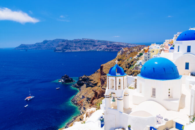 Biela kupola a zvonica s výhľadom na modré more v tradičnej stredomorskej dedinke na ostrove Santorini.