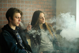 Vape teenagers.  cute girl in sunglasses and young handsome guy smoke an electronic cigarettes in the vape bar. Bad habit that is harmful to health.