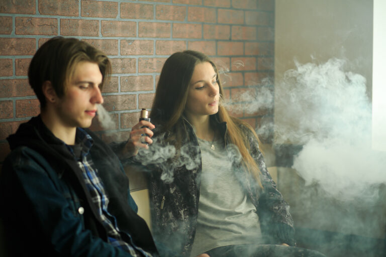 Vape teenagers.  cute girl in sunglasses and young handsome guy smoke an electronic cigarettes in the vape bar. Bad habit that is harmful to health.