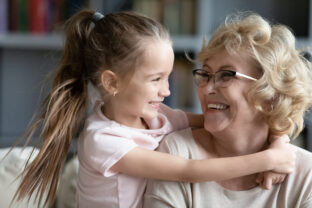 Affectionate little child girl cuddling smiling older retired grandmother.