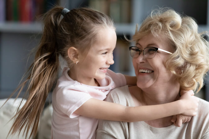 Affectionate little child girl cuddling smiling older retired grandmother.