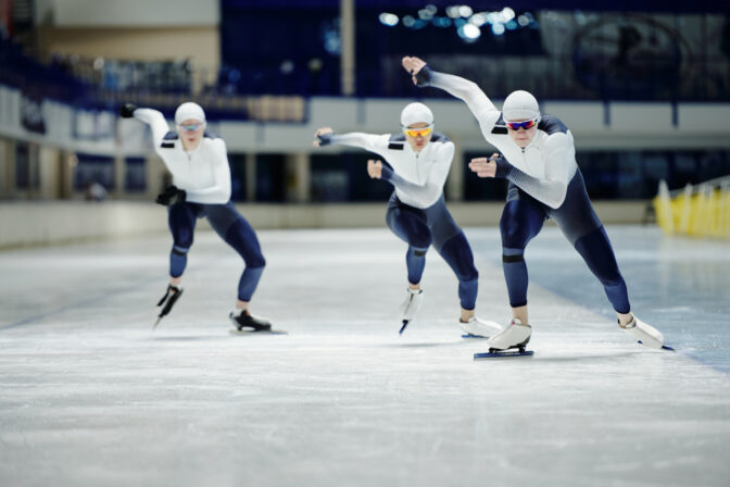 Group of young athletes speed skating with one of them sliding in front