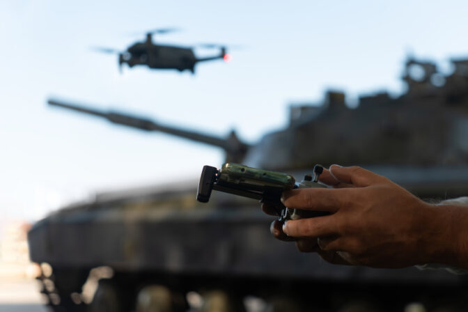 Man with a UAV control panel in his hands, a drone flying above the tank in the background in nature. help of reconnaissance drones in modern warfare.