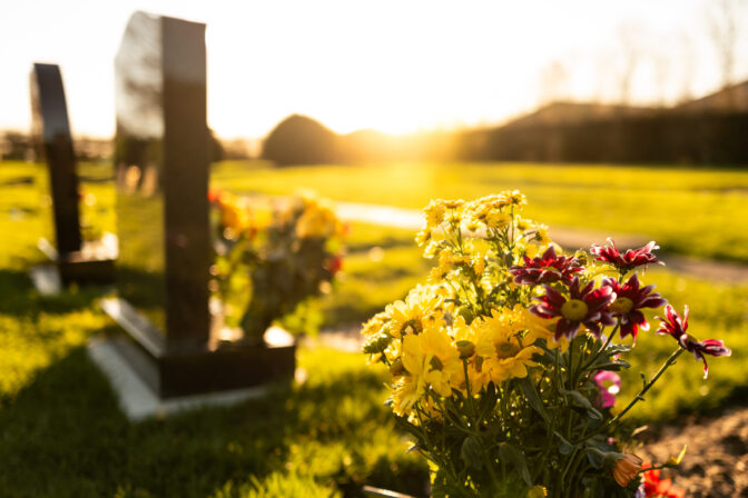 Dusk at a winter's English cemetery seen with in focus flowers in a burial plot.