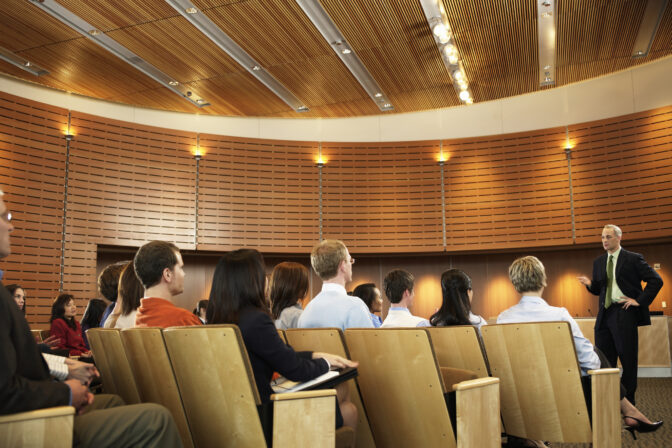 Group of executives listening to man leading seminar in auditorium