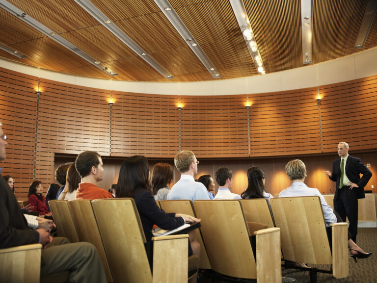 Group of executives listening to man leading seminar in auditorium