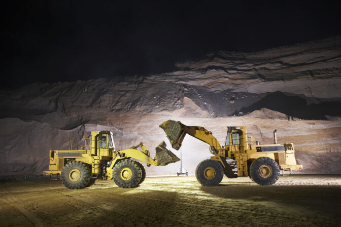 Two large bulldozers with extended shovels on floor of sand mine