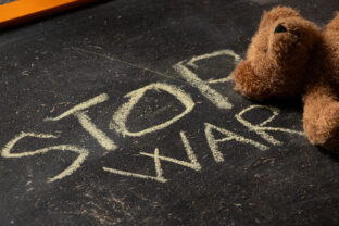 The phrase stop war is written on a black school board and a brown children's teddy bear lies nearby