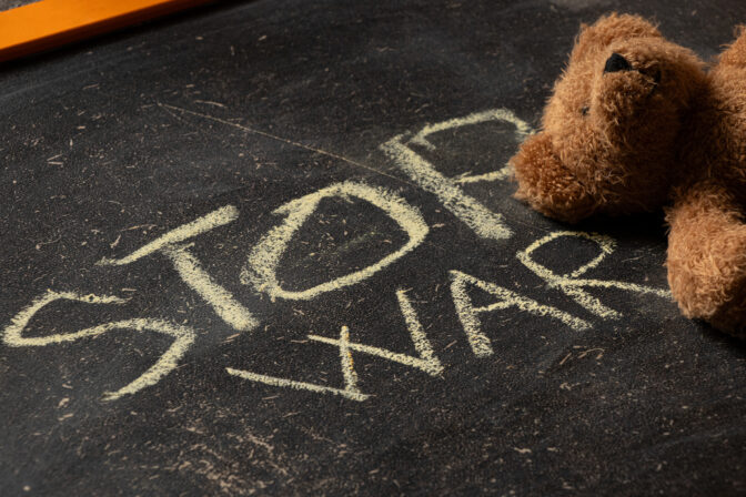 The phrase stop war is written on a black school board and a brown children's teddy bear lies nearby
