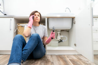 Woman sitting near leaking sink in laundry room calling for help