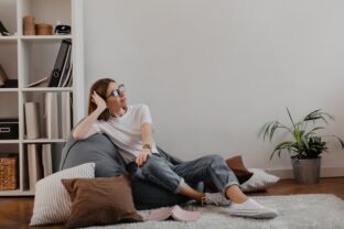 Satisfied woman in jeans and T shirt relaxed sitting in bag chair against background of shelf with folders.