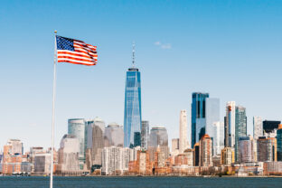 American national flag on sunny day with New York city Manhattan island in background. America cityscape, or United States nation symbol concept