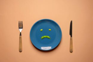Diet or Anorexic in Health Care Concept. Eating Disorder. Try to Lose Weight. Green Soy Bean on Plate Surrounded by Fork and Knife.  Unhappy Food. Top View