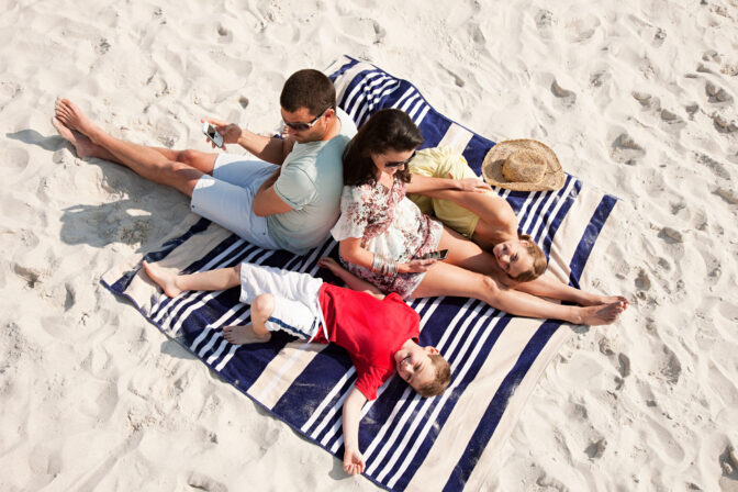 Family sitting and lying together on a rug on a beach