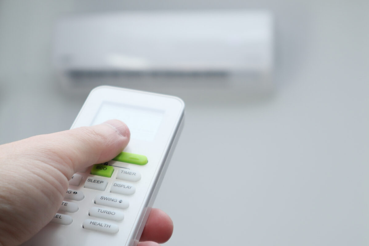 Man&#039;s hand using remote controler. Hand holding remote and adjusting temperature of air conditioner mounted on a white wall.