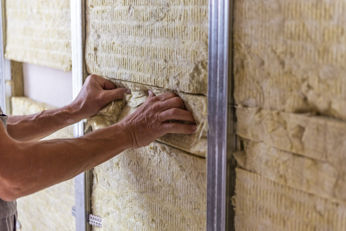 Worker insulating a room wall with mineral rock wool thermal insulation.
