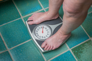 A severely overweight person weighing herself or himself on a bathroom scale
