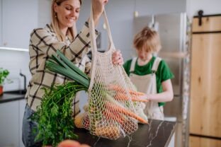 Mother bringing shopping in mesh bag to kitchen. Zero waste and sustainable packaging concept.