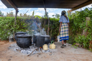 African woman, cooking in few Big pots outdoors