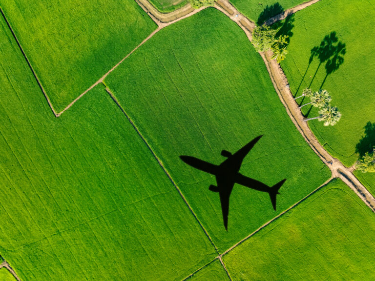Shadow airplane flying above green field. Sustainable aviation fuel. Sustainable transportation and eco friendly flight with biofuel use. Aviation sustainability. Air travel. Reduce carbon footprint.
