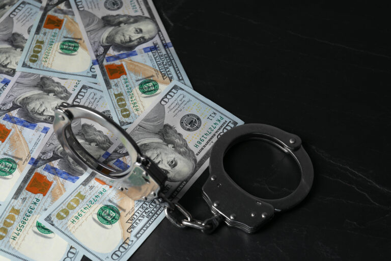 Corruption. Handcuffs and dollar banknotes on black table, closeup
