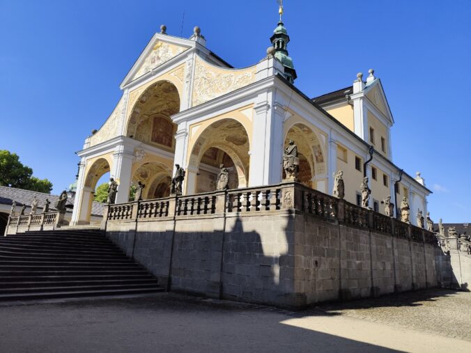 Svatá Hora - s bohato zdobenými arkádami, sochami svätcov a modrou oblohou v pozadí.