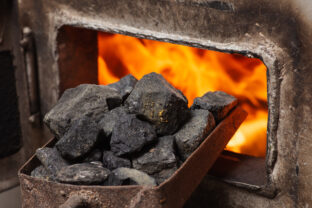 Solid fuel boiler with opened door and fire inside, scoop with coal nearby