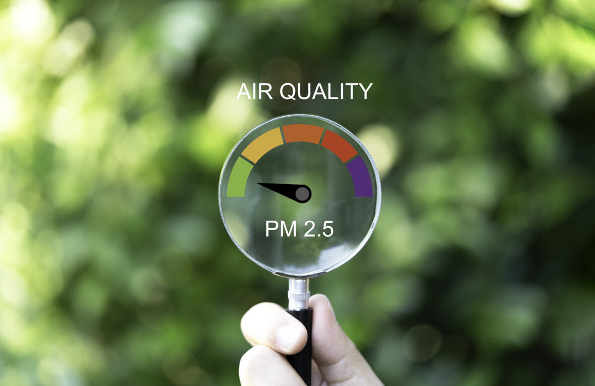 Hand holding magnifier glass with good air quality indicator scale on greenery background which check PM 2.5 or particulate matter 2.5 micron for air pollution effect to health and lifestyle concept.