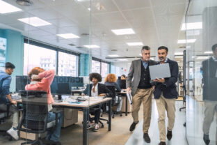 Managers using laptop while walking along computer desks in office