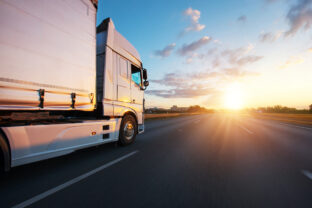 European truck driving on the asphalt road in rural landscape at sunset