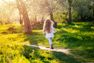 Little girl running in blooming spring garden at sunset. Back view.