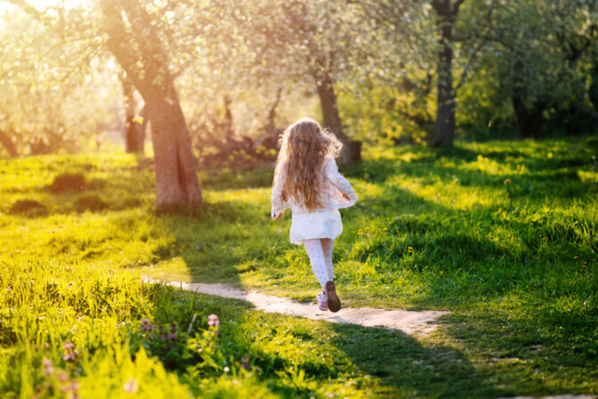 Little girl running in blooming spring garden at sunset. Back view.