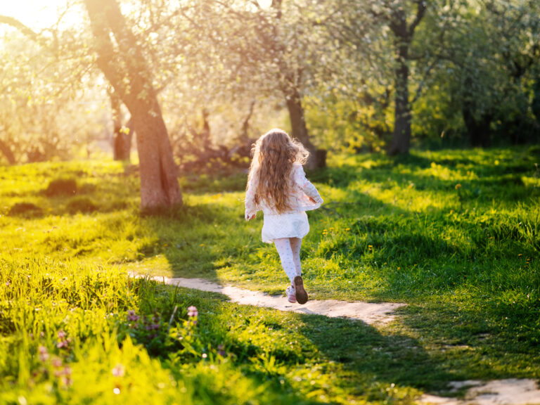 Little girl running in blooming spring garden at sunset. Back view.