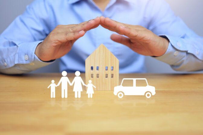 Life insurance concept with businessman using his hands to protect his family home and car, meaning to protect the health and property of the people in the home and to plan for the future.