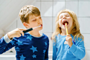 Little preschool girl and preteen school boy brushing teeth. Brother teaching sister brush teeth. Happy siblings. Two children having fun with morning dental routine. Family indoors.