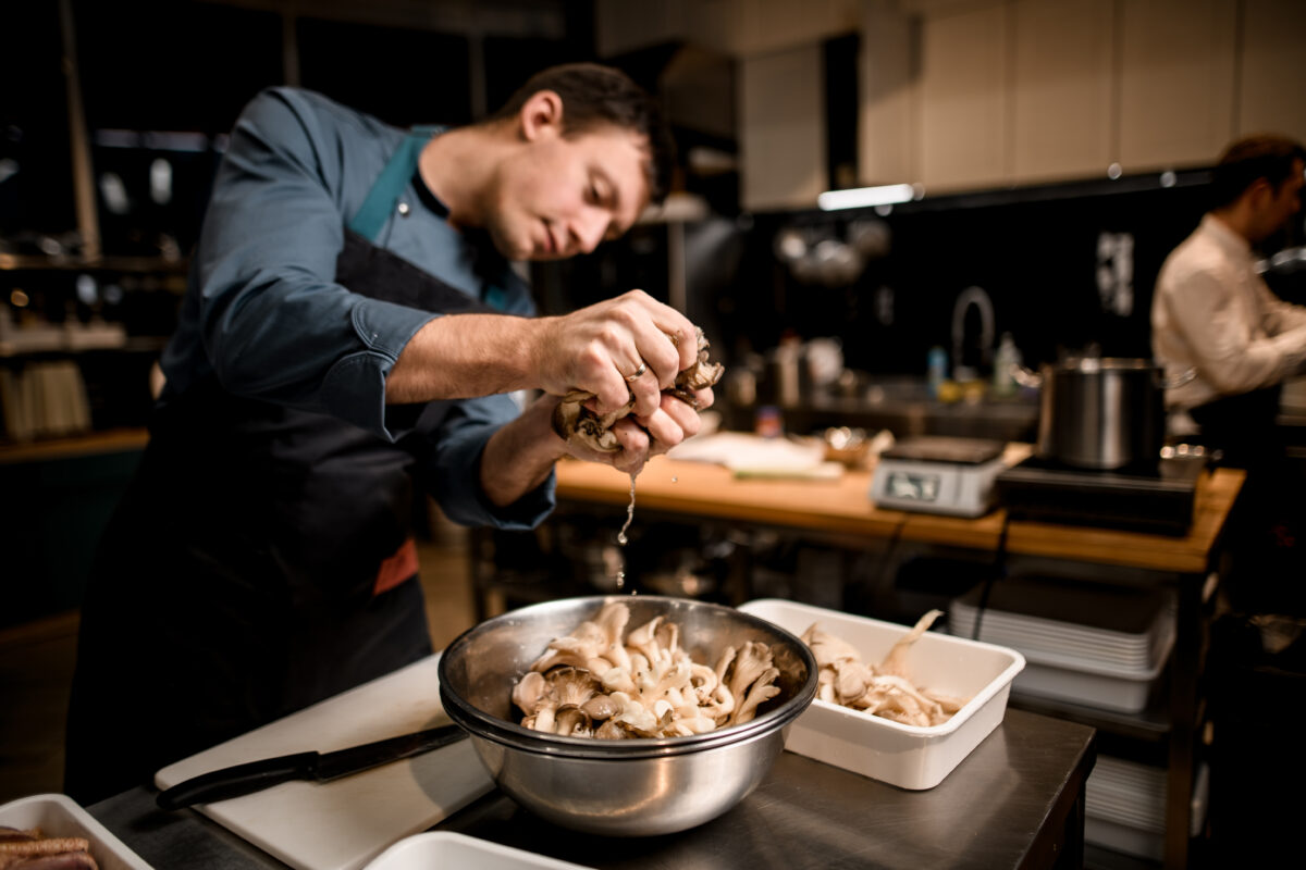 Man chef holds handful of oyster mushrooms over bowl on kitchen